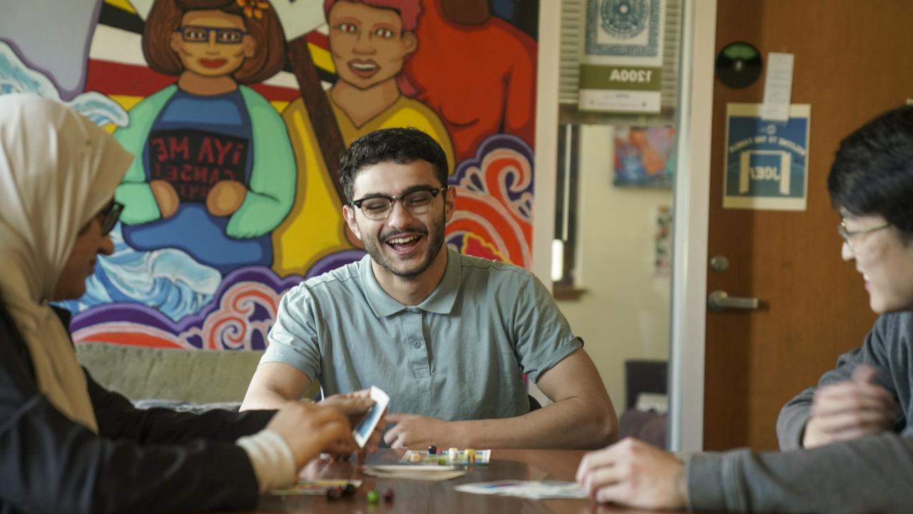 三名学生在跨文化中心的一个公共区域玩耍Lotería时谈笑风生.